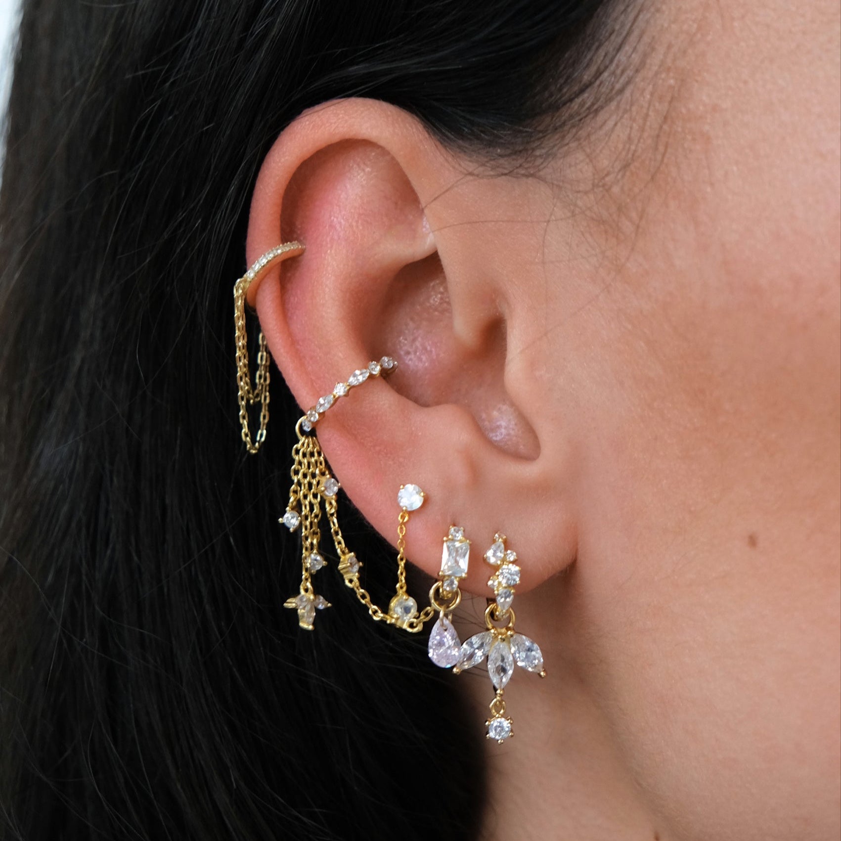 Close-up of an ear with gold earrings, chains, and a Teardrop Crystal Charm - Rose Quartz by Crystal Heaven London.