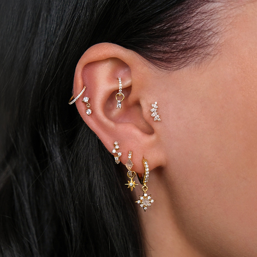 Close-up of an ear with multiple piercings, featuring gold and silver earrings, including the CHLUXE • ÉTIENNE Cartilage Stud in 14K Yellow Gold by Crystal Heaven London adorned with small star and floral designs.