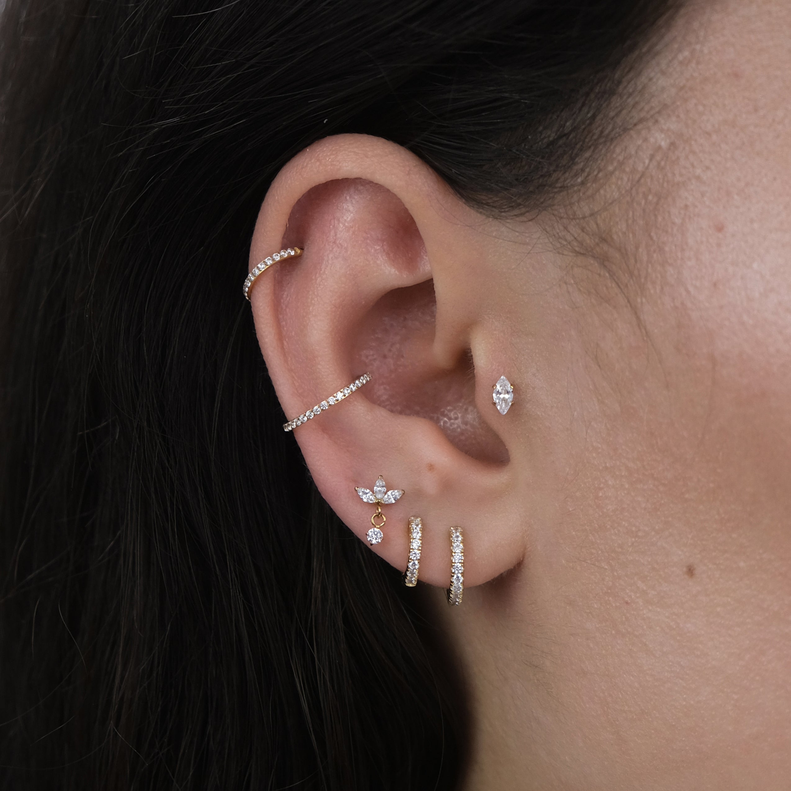 Close-up of a curated ear with multiple ear piercings and gold hoop earrings and labret earrings suitable for a tragus, helix, lobe and conch piercing.