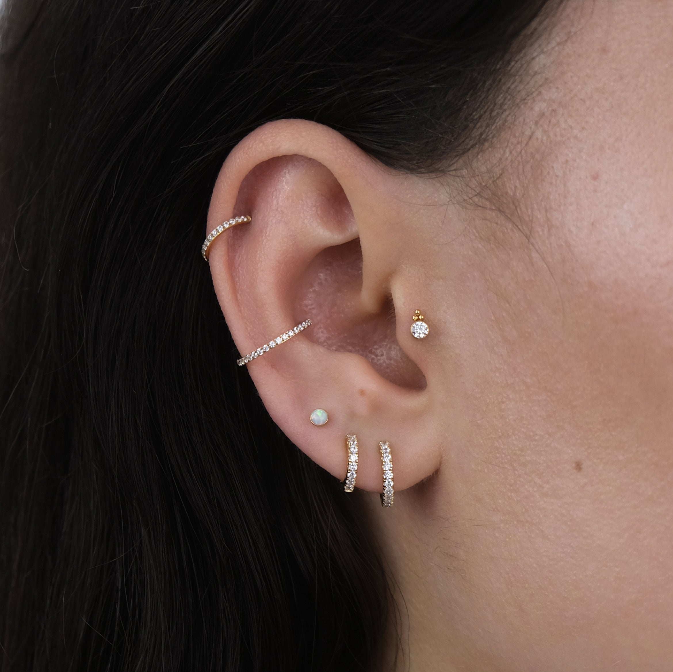 Close-up of a curated ear with multiple ear piercings and gold hoop earrings and labret earrings for a tragus, helix, lobe and conch piercing.