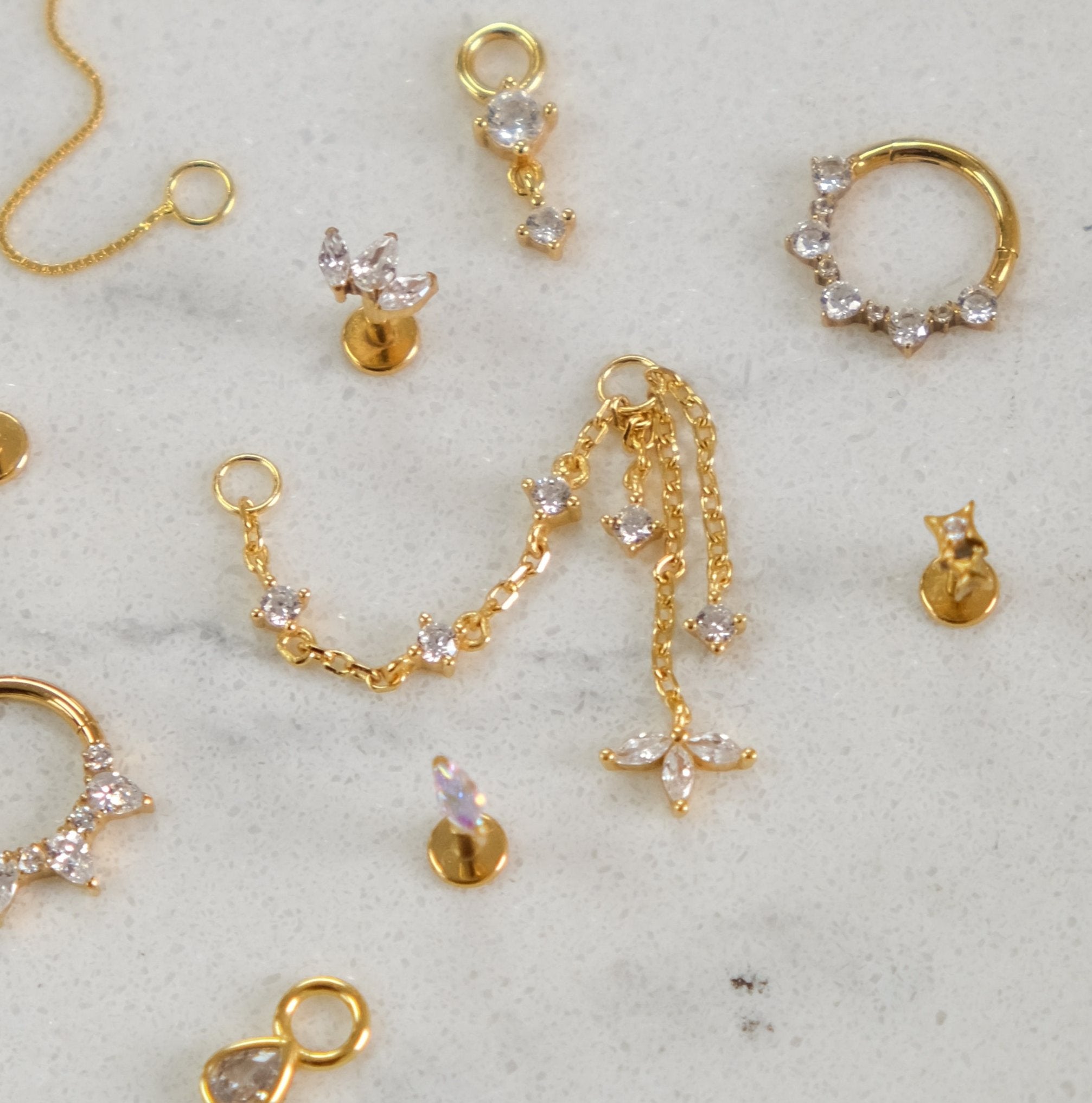 A selection of LANI Marquise Droplet Chain Charms by Crystal Heaven London, featuring gold and diamond earrings and pendants, showcased on a light surface.