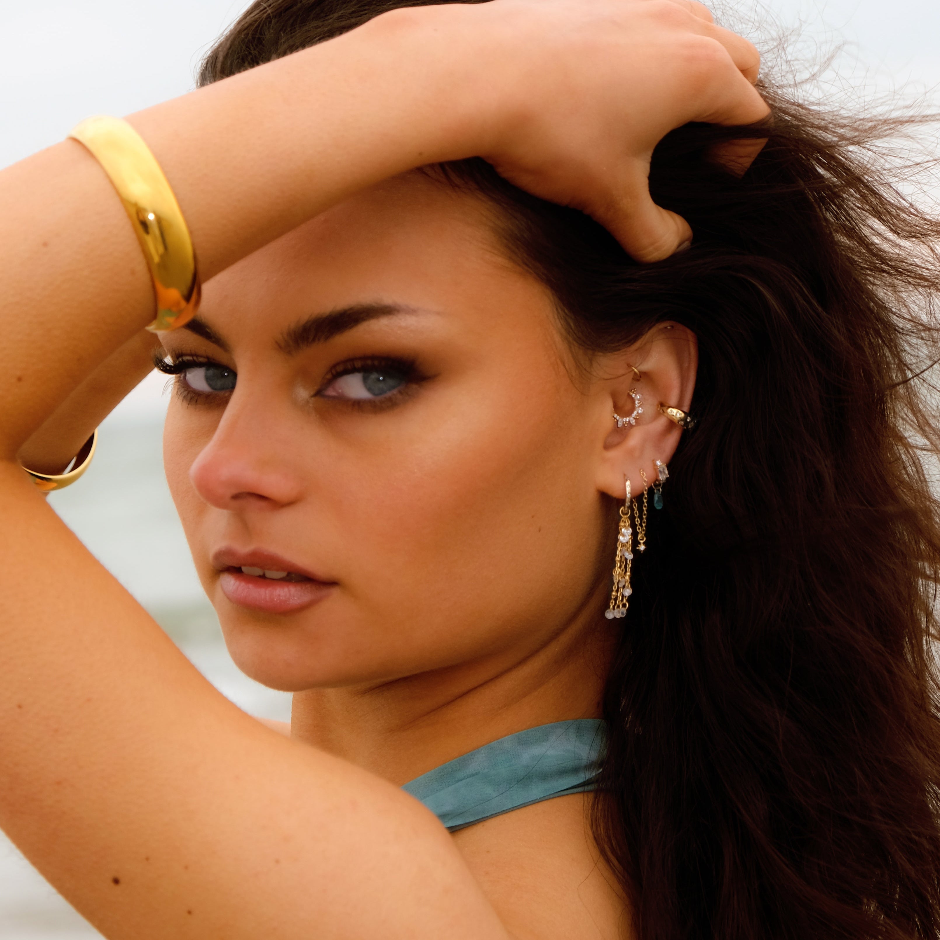 Woman with long dark hair wears gold jewelry and SOLEIA Illusion Chain Stud by Crystal Heaven London.