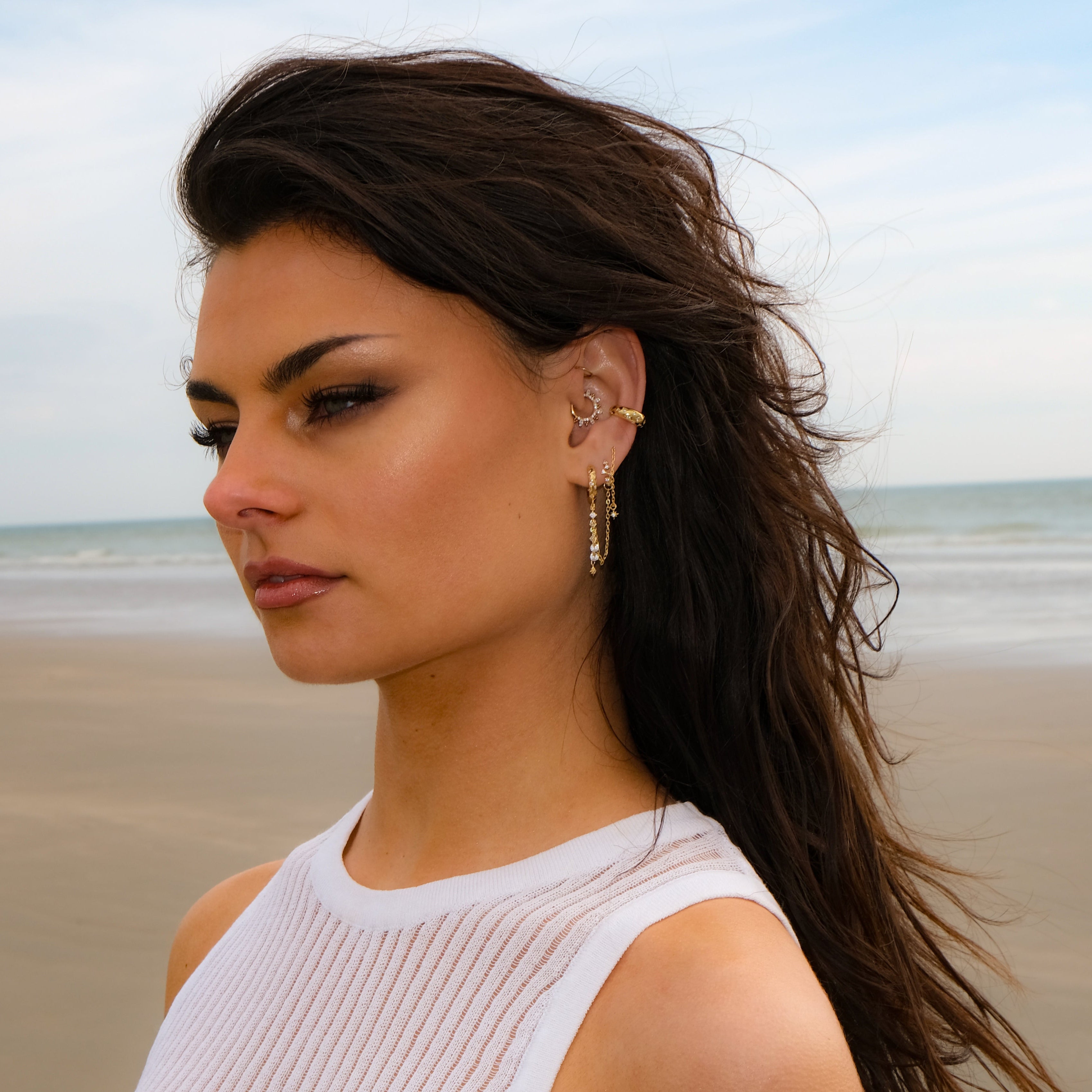 Woman with long dark hair wears Crystal Heaven London SOLEIA Waterfall Huggie Hoops on the beach.