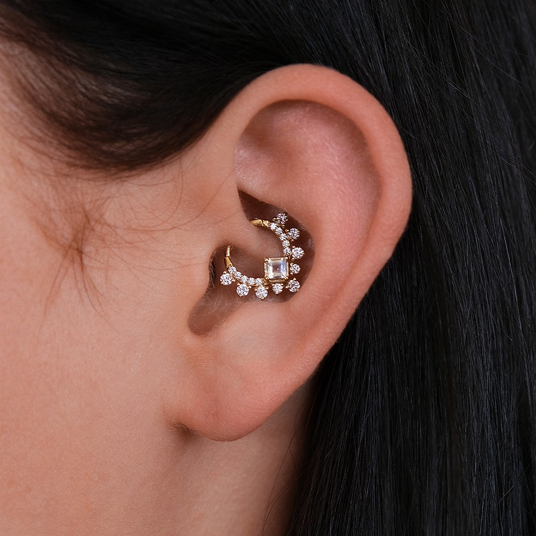 The CHLUXE • GODDESS Moonstone Daith Hoop from Crystal Heaven London, crafted in 14K yellow gold and adorned with rhinestones, brings to mind the elegance of a goddess.