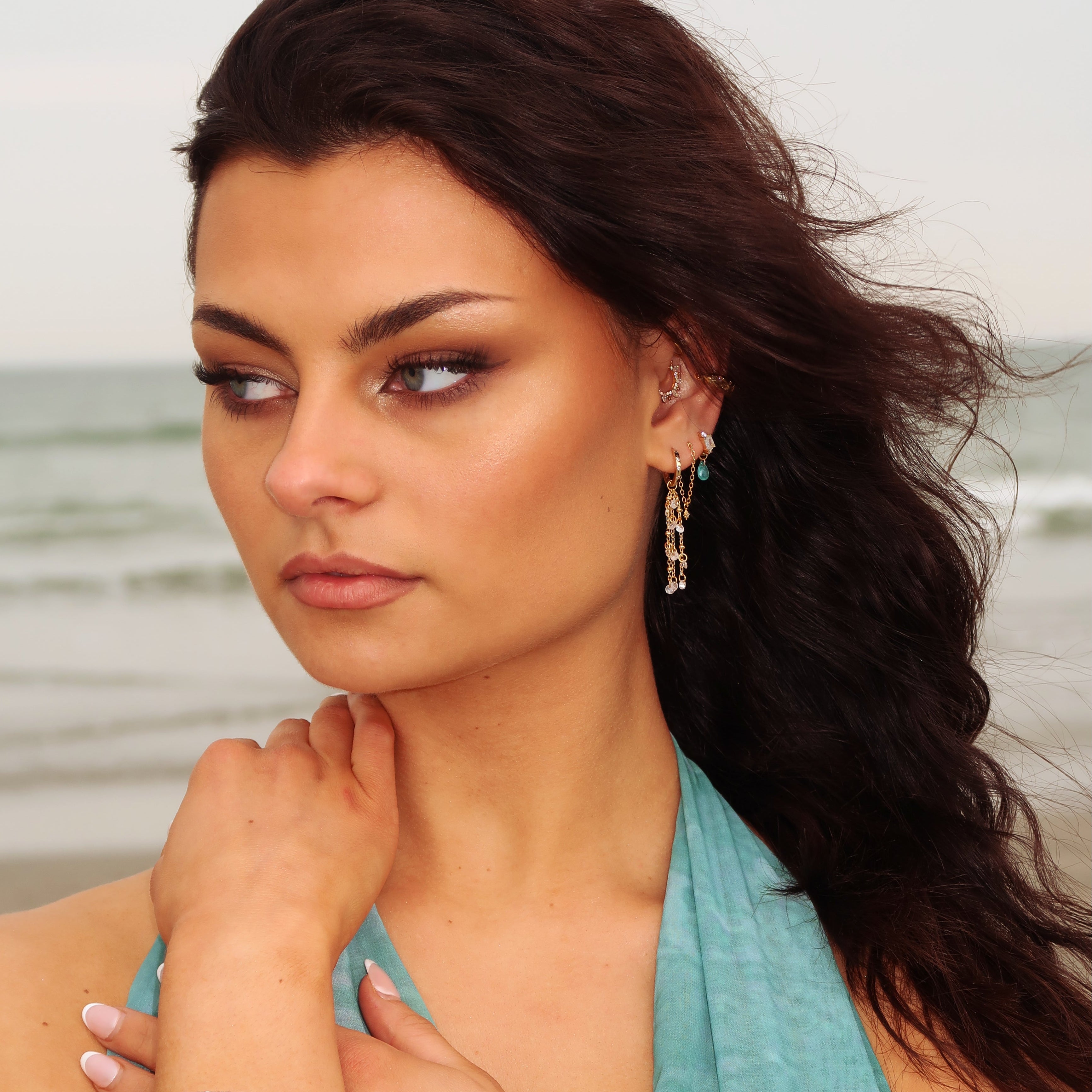 Woman with long brown hair in a blue top, wearing KAIA Waterfall Droplet Earrings by Crystal Heaven London.