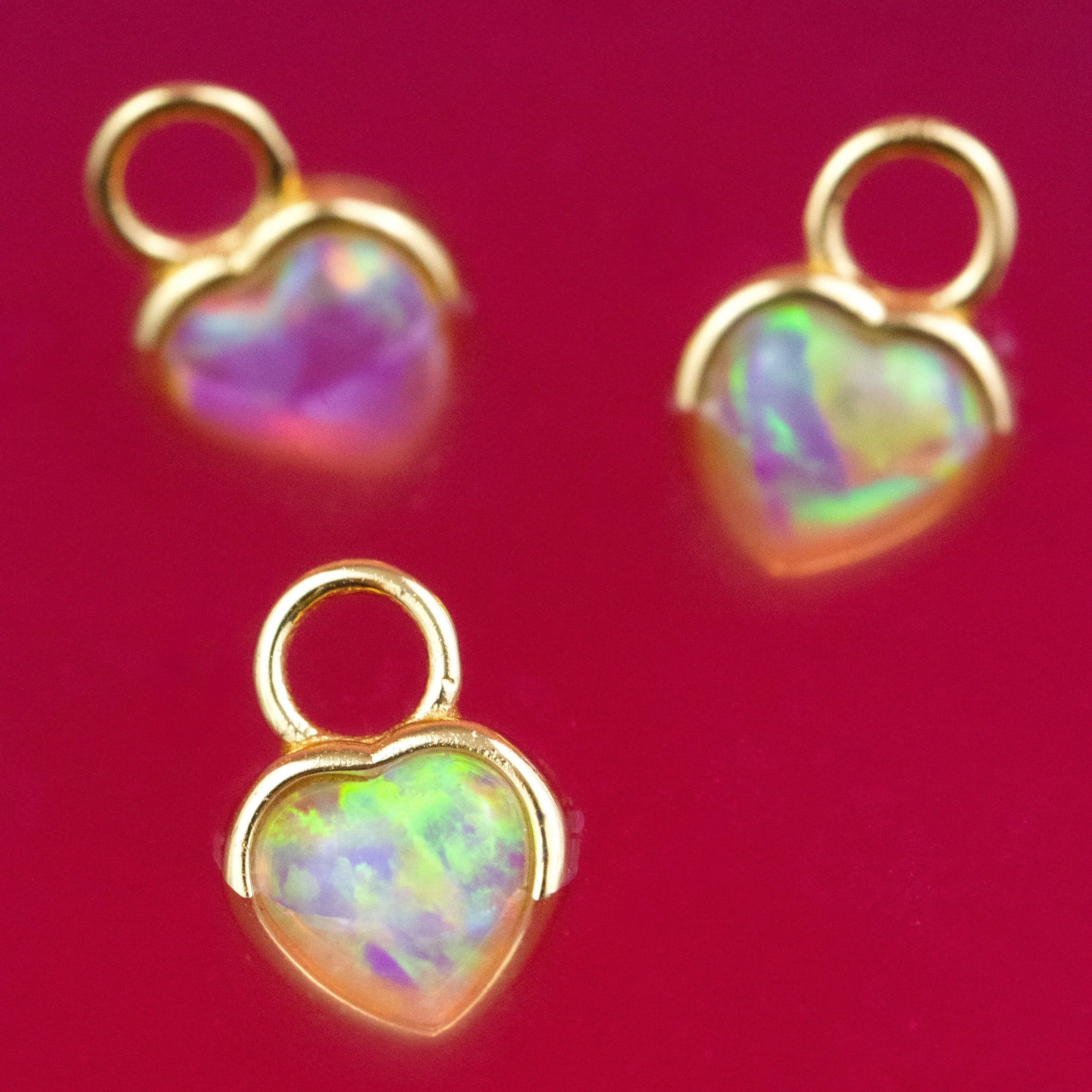 Heart-shaped opal pendants with gold frames on a red background