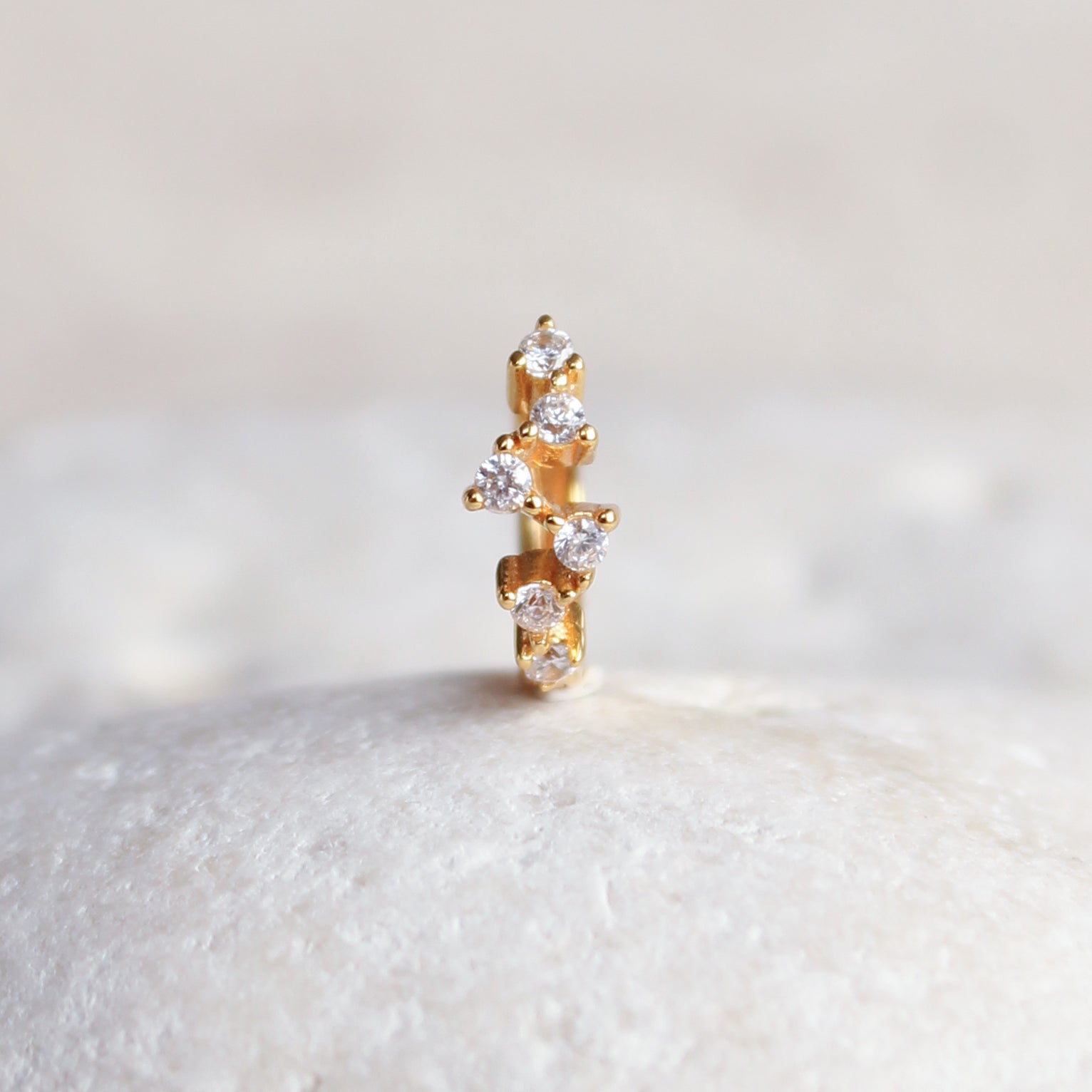 A close-up of the ESTELLA Constellation Huggie from Crystal Heaven London, featuring shimmering diamonds set vertically like scattered crystals, delicately positioned on a soft white surface.