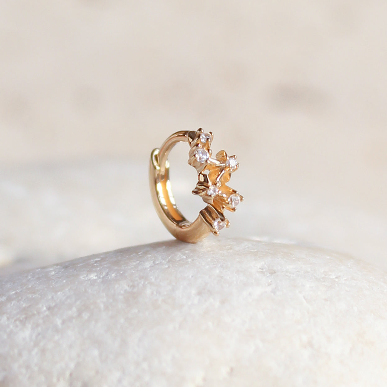 The CHLUXE Constellation Huggie Hoop by Crystal Heaven London is a celestial-inspired ring, crafted from 14K solid yellow gold, with small clustered gemstones elegantly set on a smooth white stone surface.