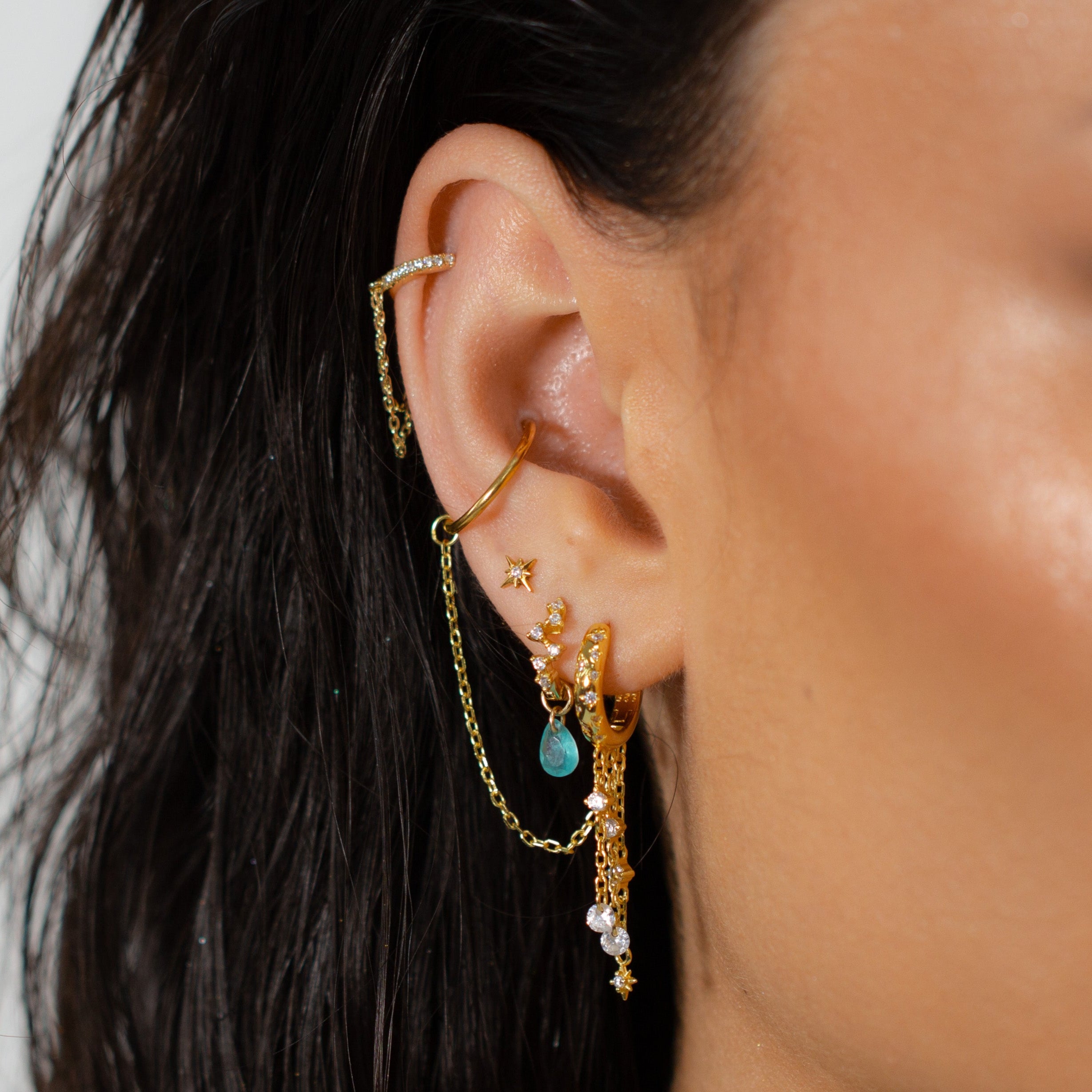 Close-up of an ear with Crystal Heaven London SOLEIA Waterfall Huggie Hoops and gold chains.