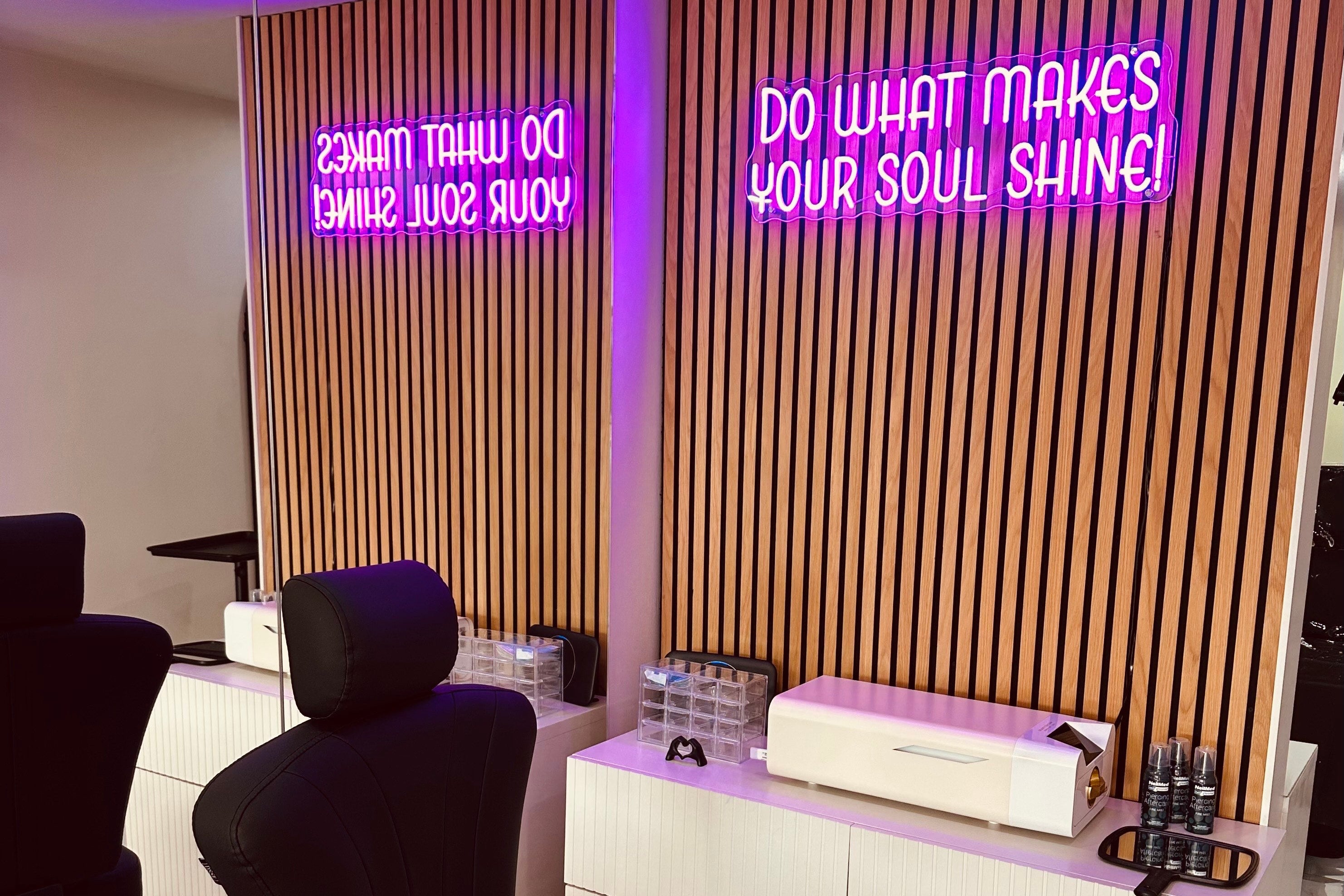 Modern piercing shop interior with black chairs and a white counter, illuminated by purple neon signs.