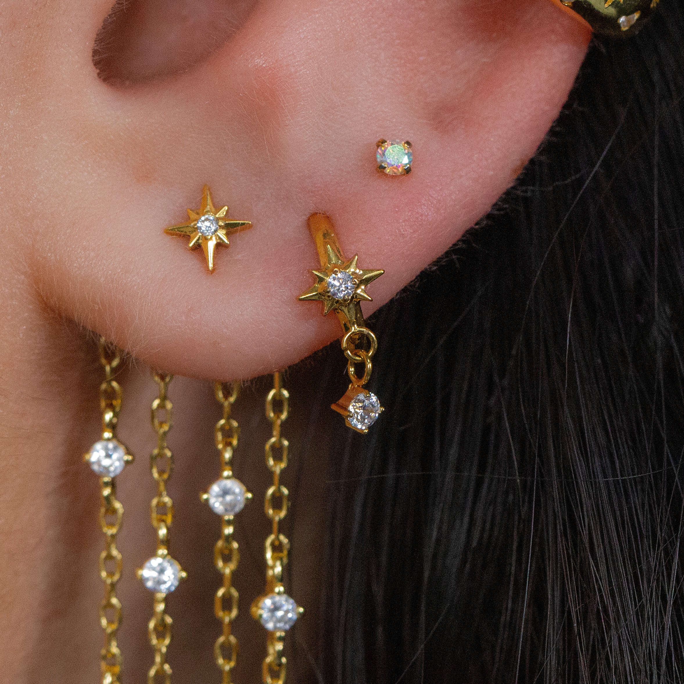Close-up of an ear with multiple earrings, featuring the SOLEIA Droplet Cartilage Hoop by Crystal Heaven London.