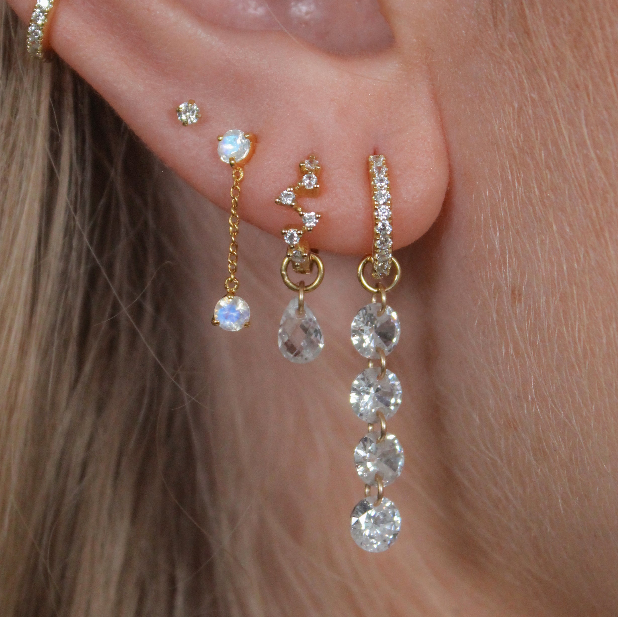 Close-up of an ear with gold and crystal earrings.
