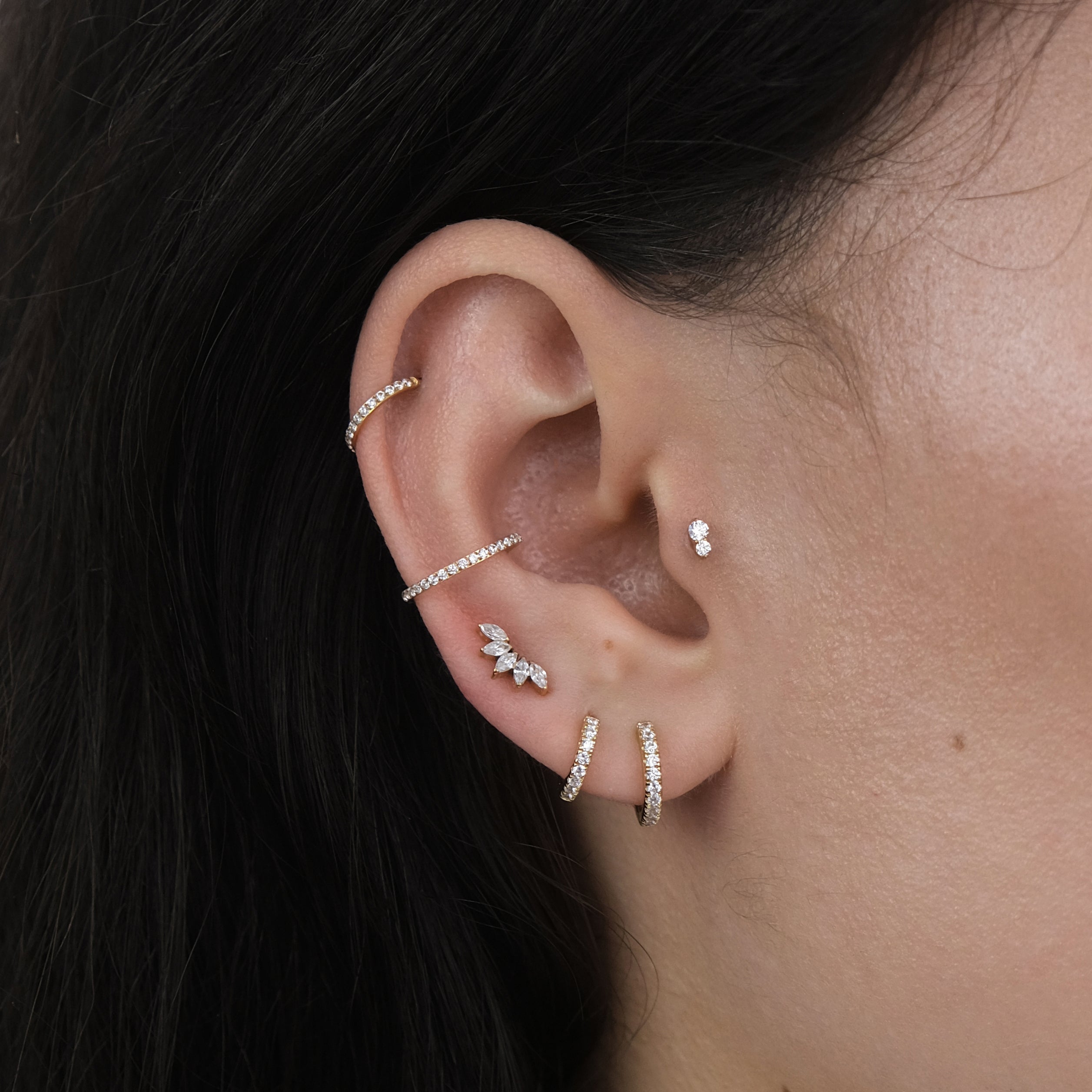 Close-up of a curated ear with multiple ear piercings and gold hoop earrings and labret earrings for a tragus, helix, lobe and conch piercing.