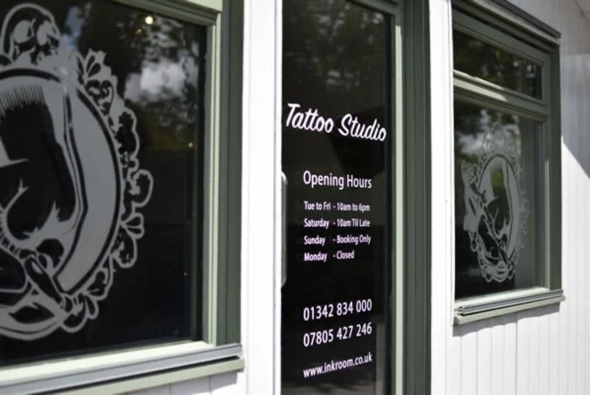Tattoo studio window with opening hours and contact information displayed.