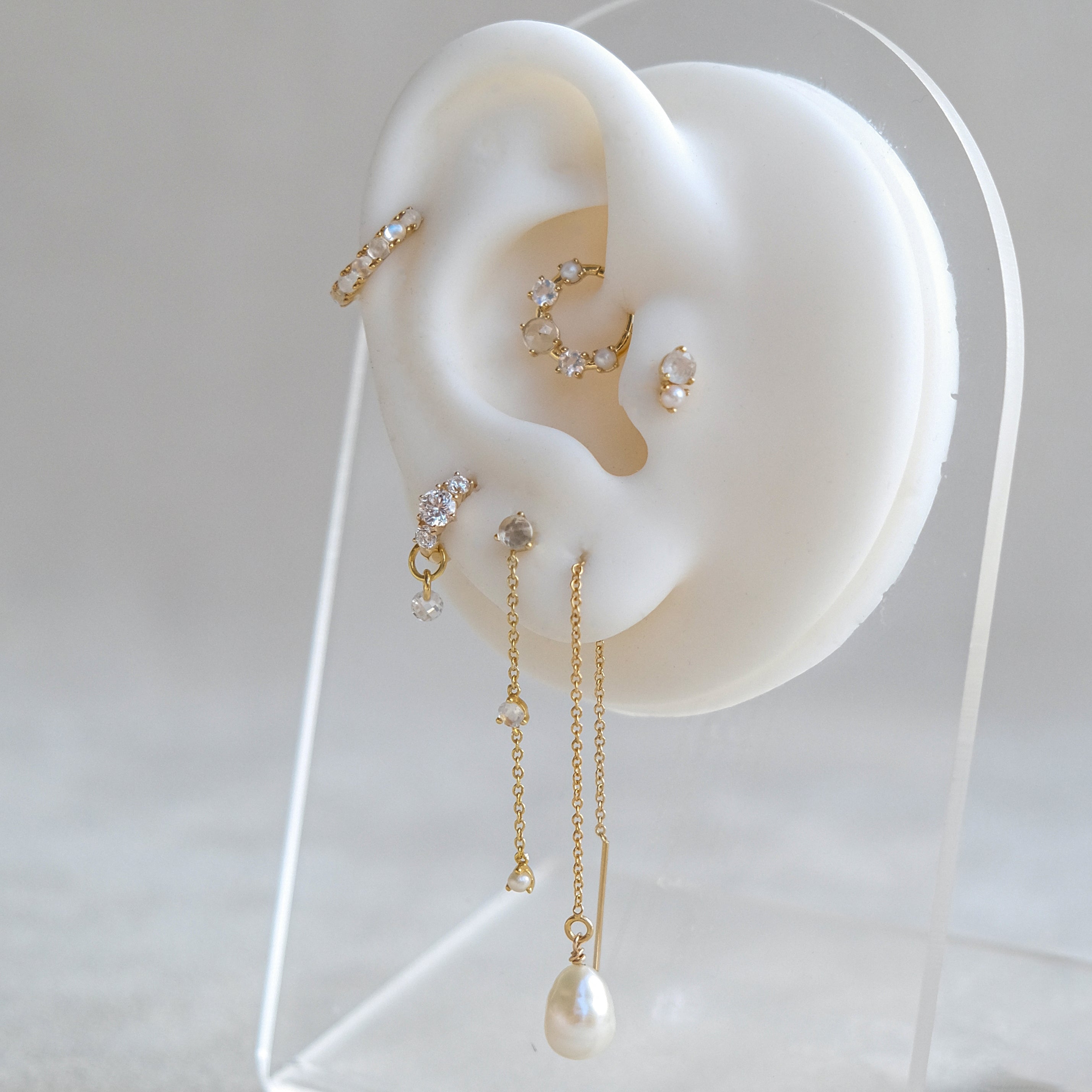 On a white mannequin ear, Crystal Heaven London showcases the OPHELIA Gemstone Waterfall Studs—a stunning display of gold earrings adorned with shimmering pearls, crystals, and rose-cut white topaz.
