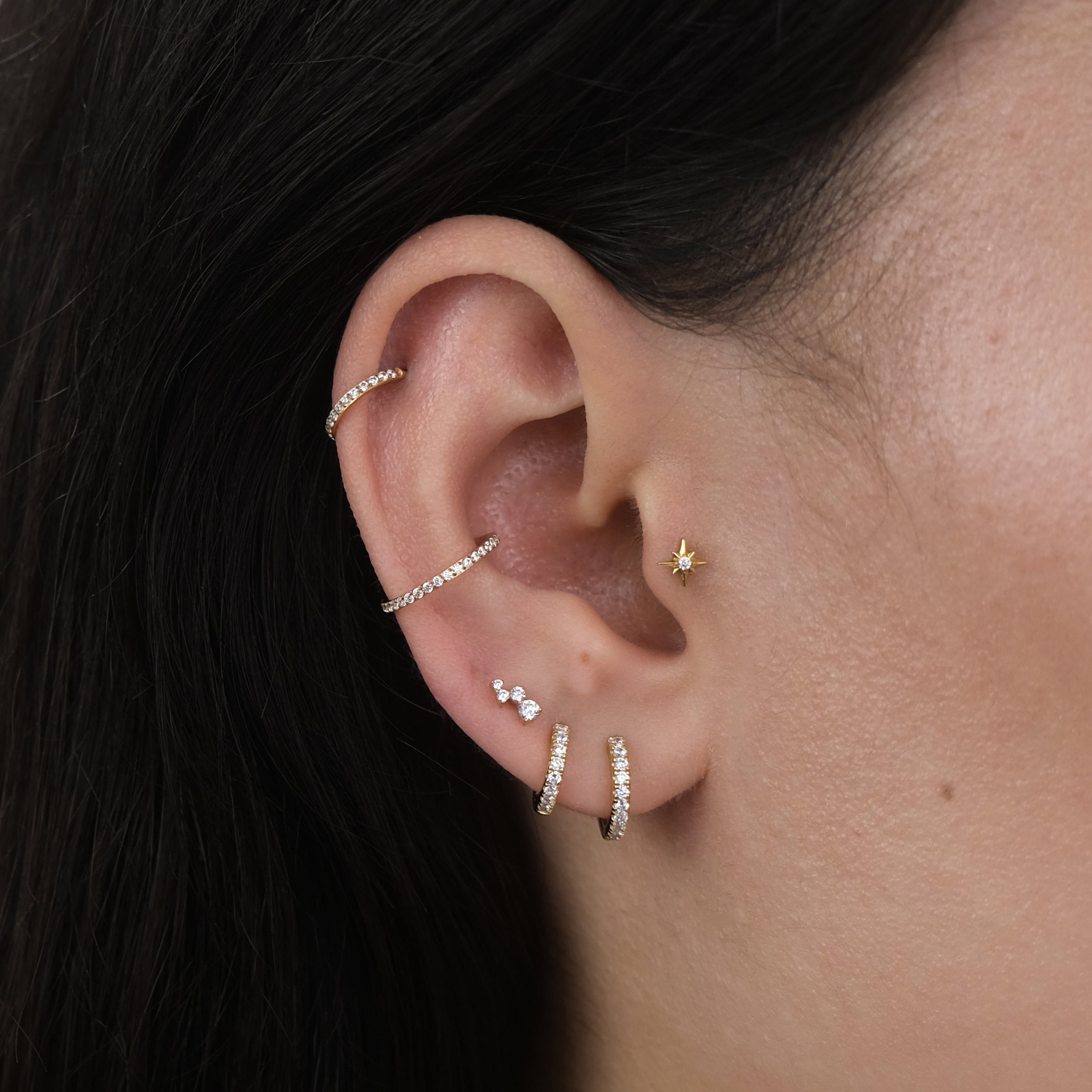 Close-up of a curated ear with multiple ear piercings and gold hoop earrings and labret earrings for a tragus, helix, lobe and conch piercing.