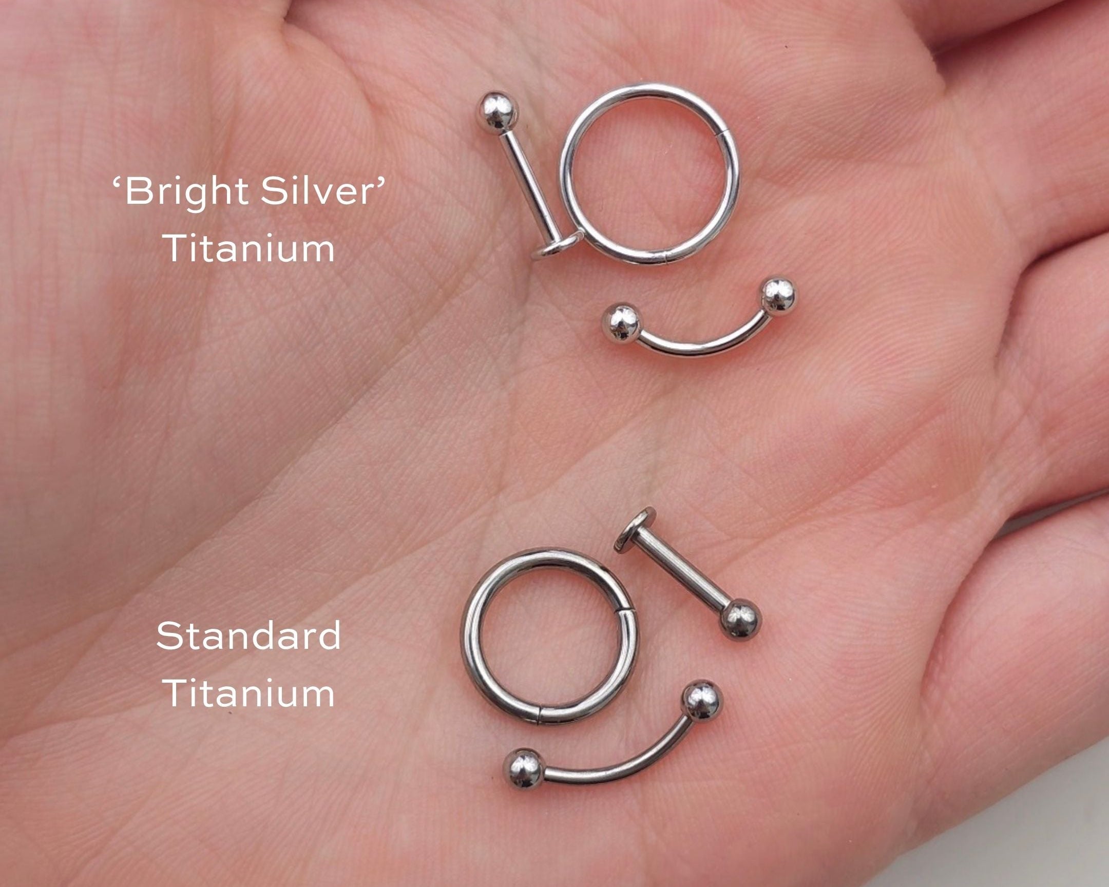 Two pairs of titanium nose rings, one labeled 'Bright Silver' and the other 'Standard Titanium', held in a hand.