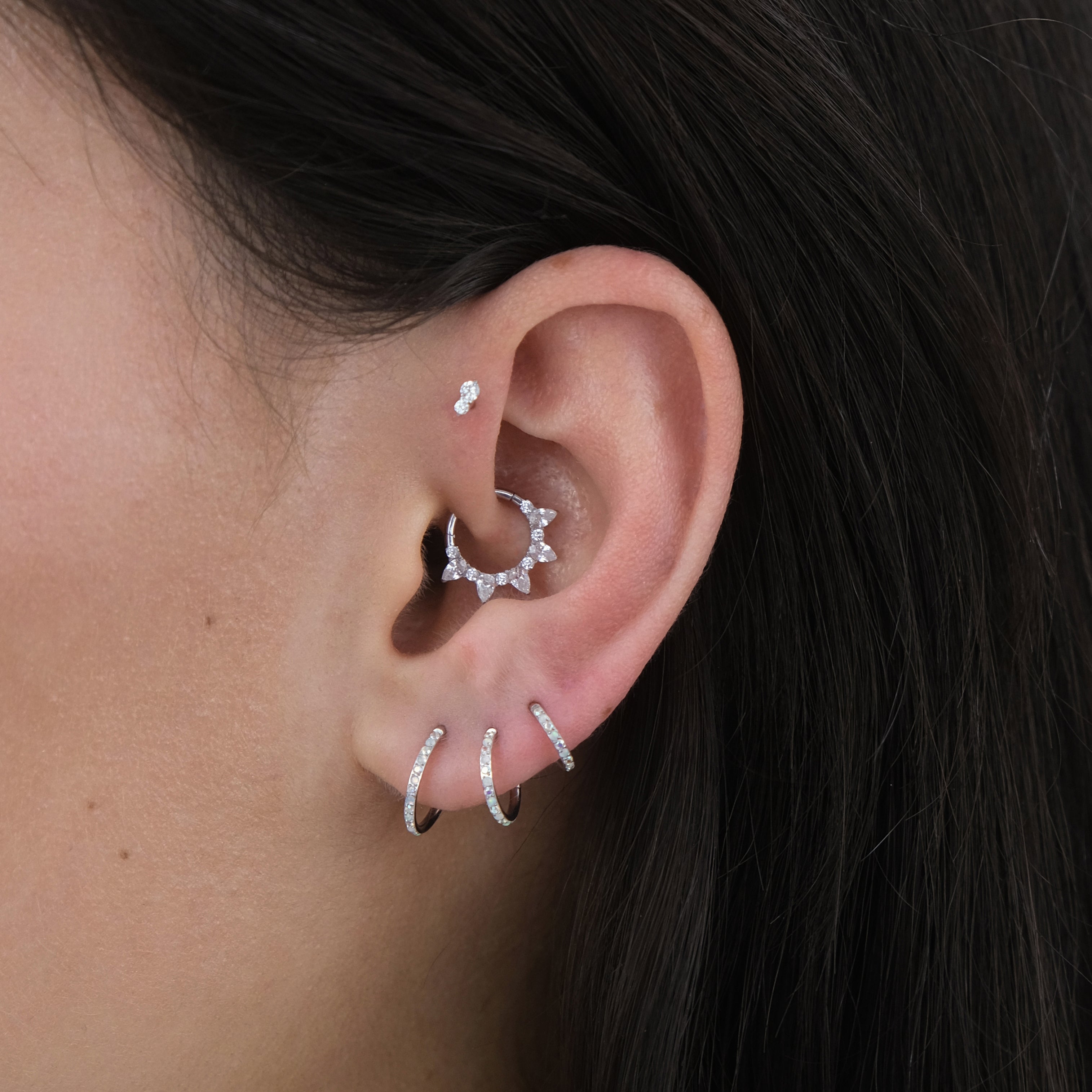 Close-up of a curated ear with multiple ear piercings and silver hoop earrings and labret earrings for a tragus, helix, lobe and conch piercing.